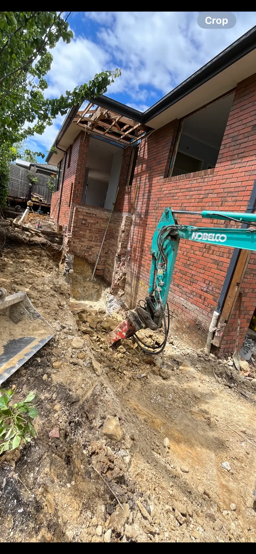 Underpinning excavation — Rock breaking and foundation dig alongside an existing brick home
