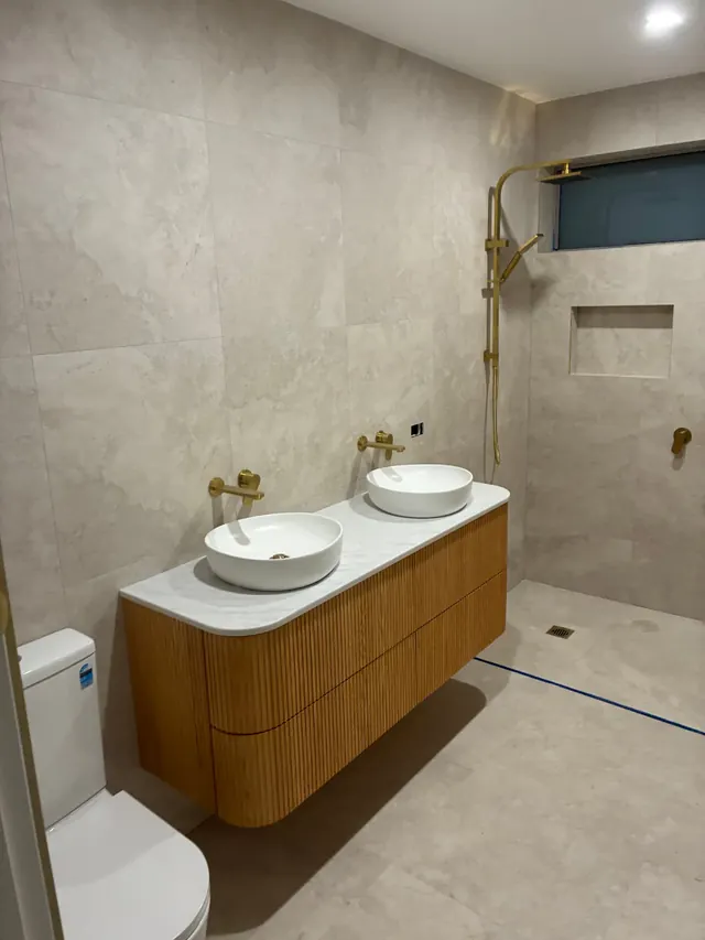 Bathroom vanity fit-off — Timber vanity with twin basins, marble top and brass tapware set off in a fully tiled bathroom
