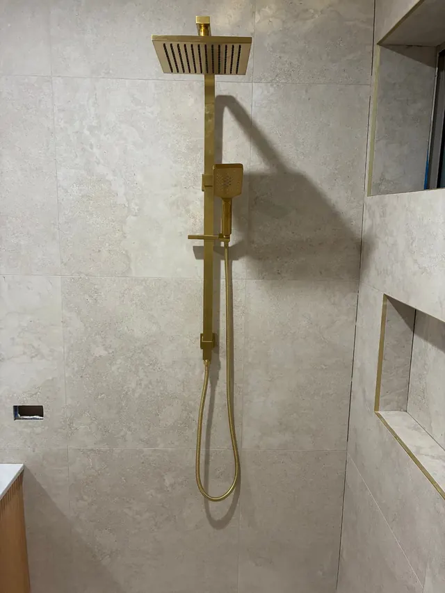 Brass shower set installation — Brushed brass twin shower set with rain head and handpiece, installed flush to tiled walls