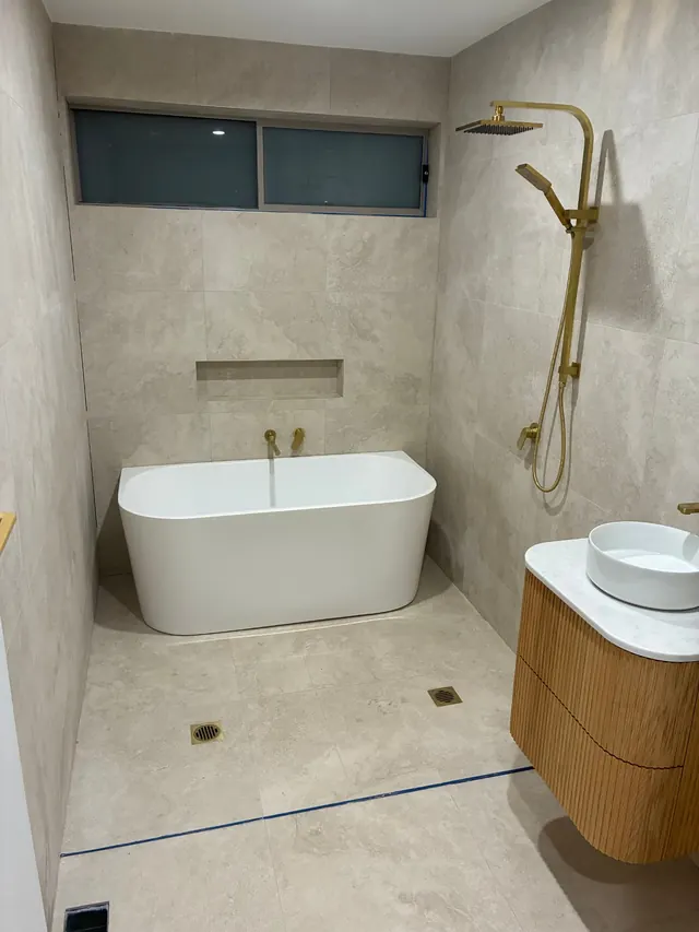 Freestanding bath installation — Freestanding bath with brass wall mixers, set under a feature window in a tiled ensuite