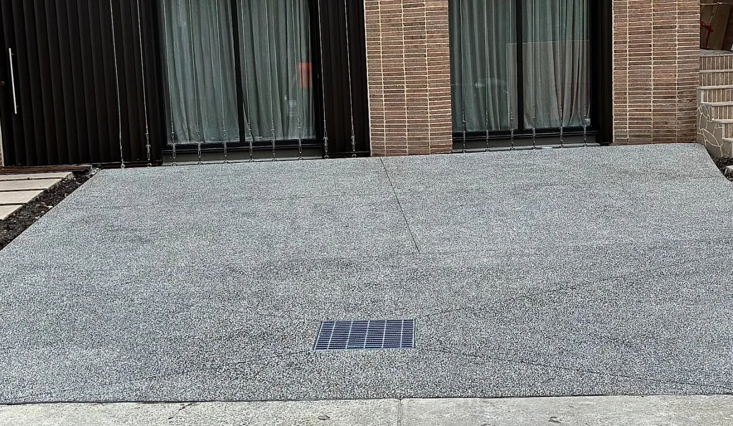 Precision exposed aggregate driveway with an integrated drainage grate at the base of a new home