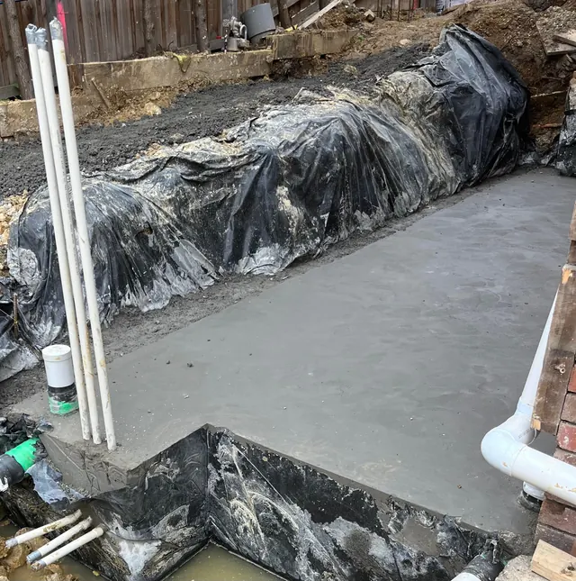 Extension slab pour — Reinforced extension slab poured over vapour barrier with plumbing and conduit set in place